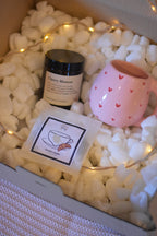 Coffret cosy contenant un mug artisanal, du thé bio au caramel et une bougie en cire de soja avec mèche en coton dans un pot en verre, le tout accompagné d’une guirlande lumineuse