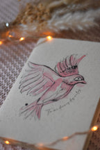 Carnet de notes posé sur un plaid rose, entouré d’une guirlande lumineuse et de fleurs séchées.