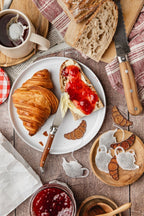 Sachet de thé en forme de théière et petit croissant pailleté, dans une ambiance de petit-déjeuner gourmand avec croissants, pain, confiture et tasse de thé.